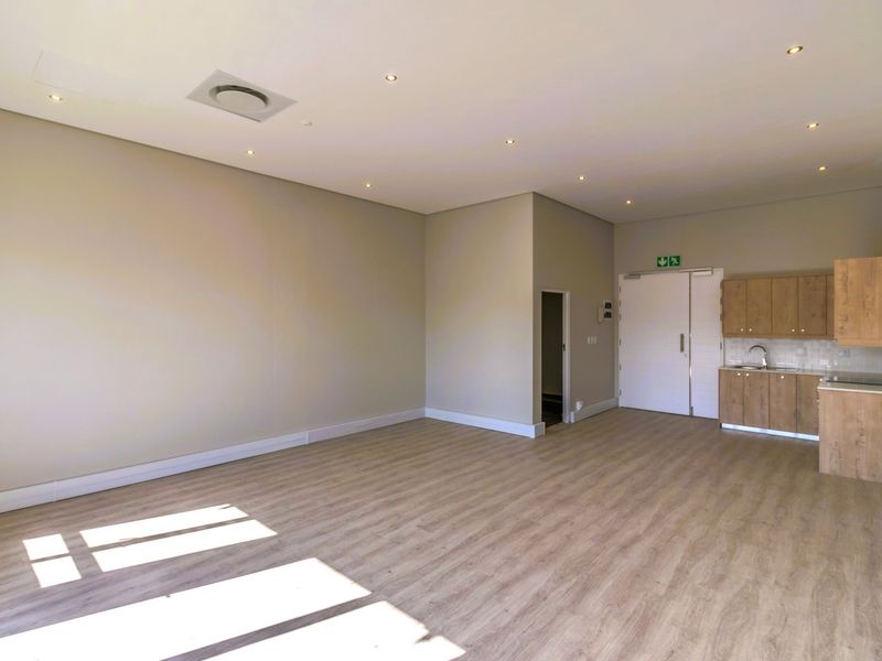 A bright, open-plan commercial space featuring modern laminate flooring, recessed lighting, and a compact kitchenette with built-in cabinetry and a sink.
