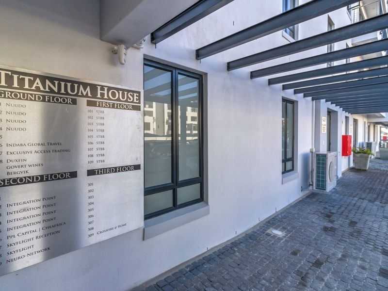 Exterior view of Titanium House featuring a metal directory sign, paved walkway, and steel pergola structure at the building entrance.