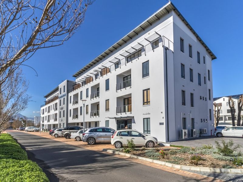 A modern multi-story commercial building featuring a clean white facade, private balconies with metal railings, and dedicated paved parking.