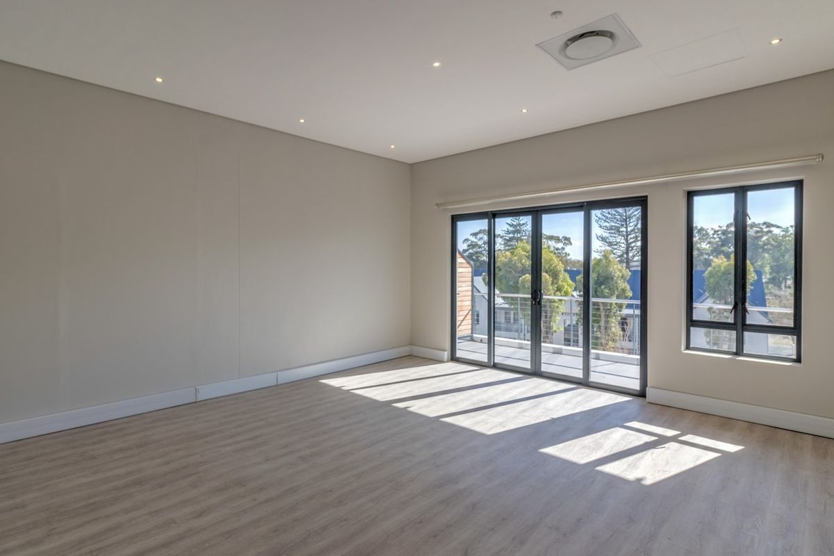 A bright, spacious, and empty living area featuring modern laminate flooring, recessed lighting, and large sliding glass doors leading to a balcony.