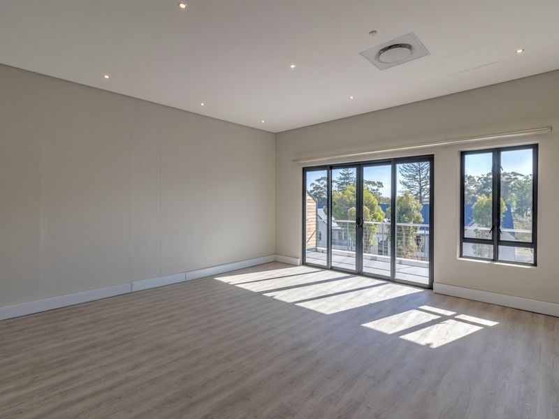 A bright, spacious, and empty living area featuring modern laminate flooring, recessed lighting, and large sliding glass doors leading to a balcony.