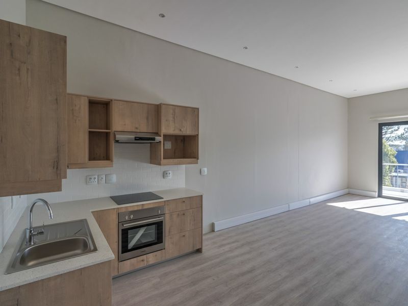 Modern open-plan kitchen and living area featuring light wood cabinetry, integrated appliances, laminate flooring, and access to a private balcony.