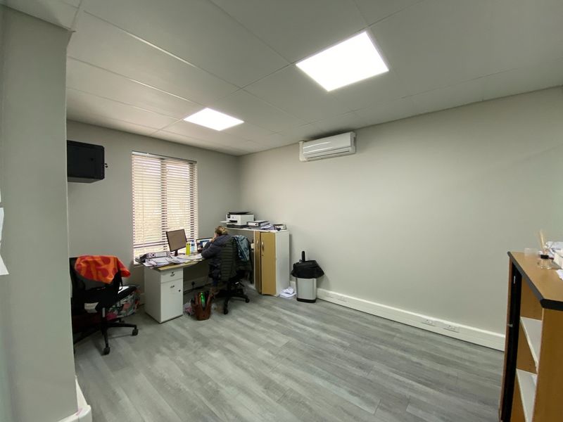 A functional office space featuring modern laminate flooring, recessed LED lighting, and a wall-mounted split-system air conditioning unit.