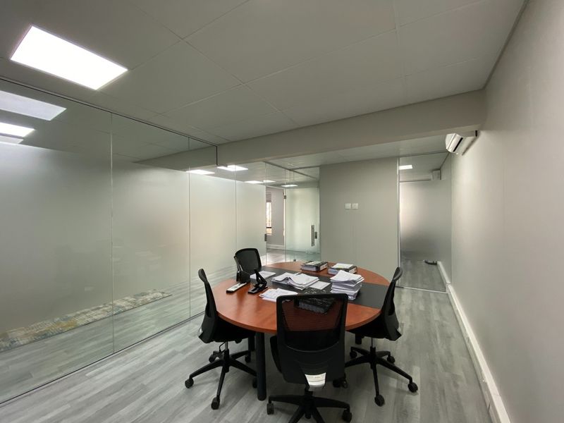 A modern office meeting room featuring glass partition walls, suspended ceiling with recessed lighting, and split system air conditioning.
