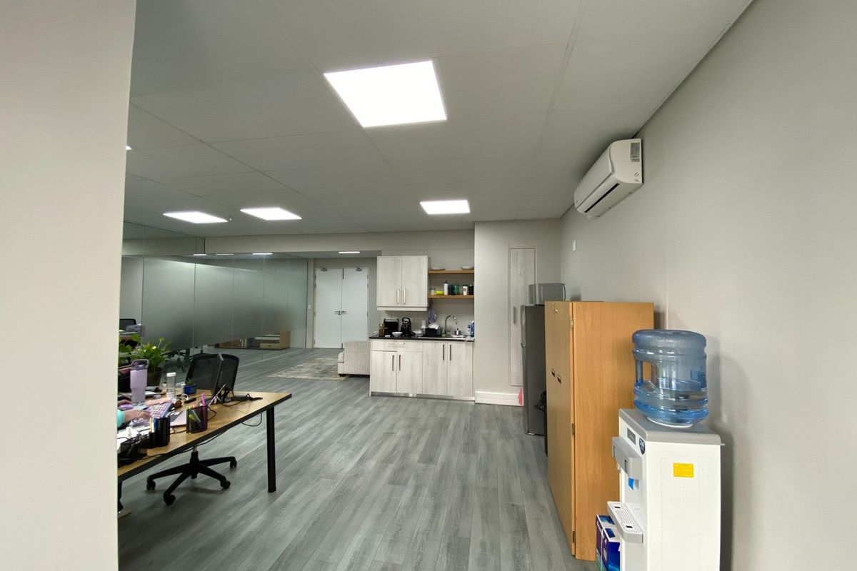 A modern office space featuring a functional kitchenette, laminate flooring, recessed lighting, and a mirrored wall, providing a clean and professional work environment.