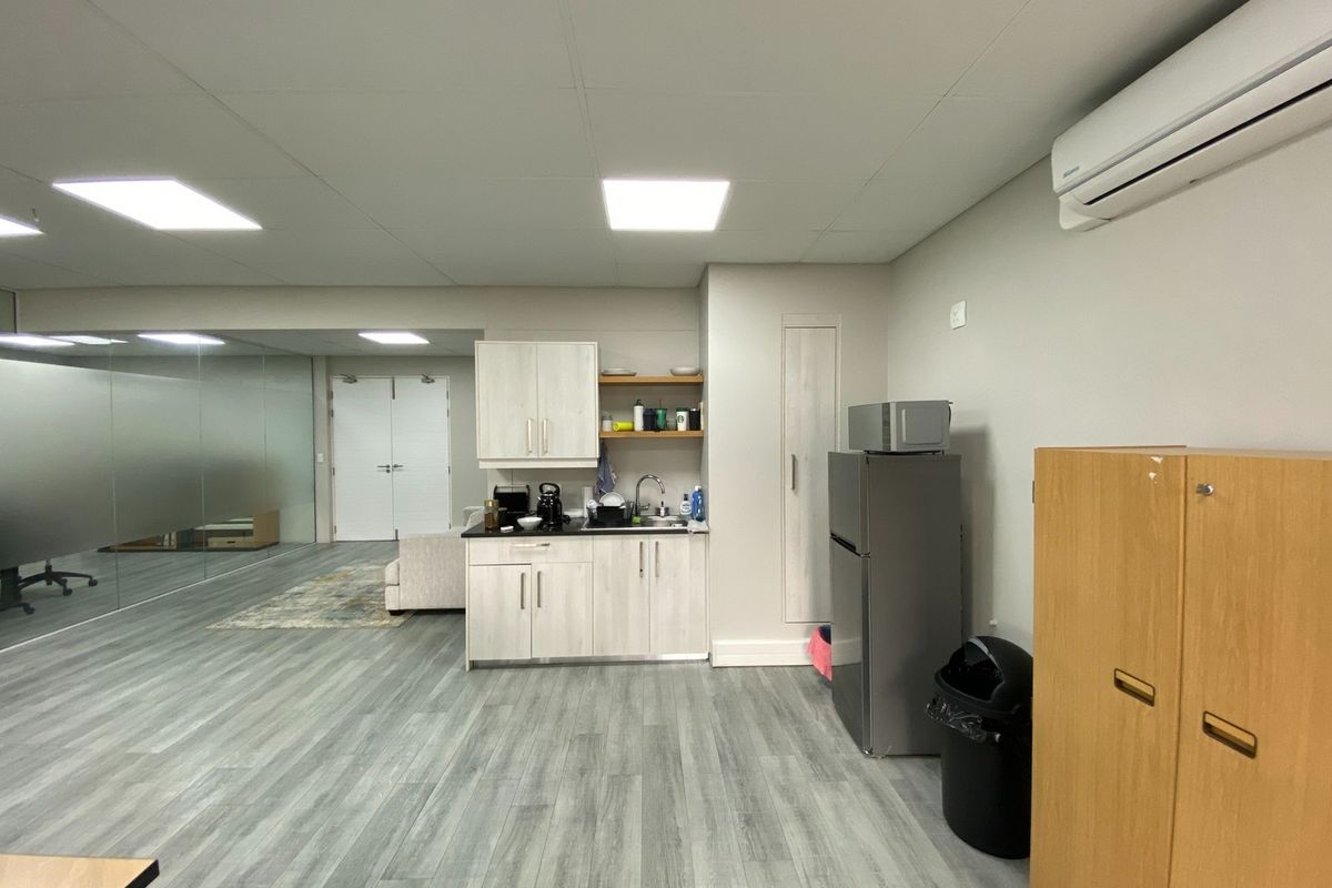 Modern office space featuring a functional kitchenette, glass partition wall, split-system air conditioning, and durable laminate flooring.