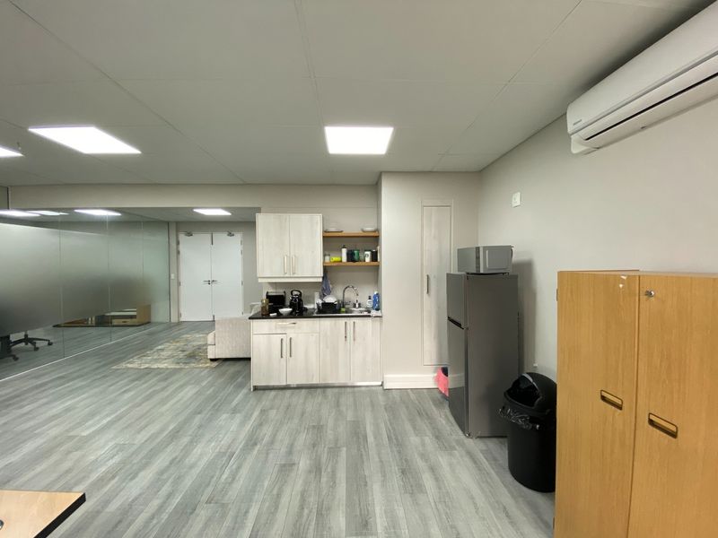 Modern office space featuring a functional kitchenette, glass partition wall, split-system air conditioning, and durable laminate flooring.