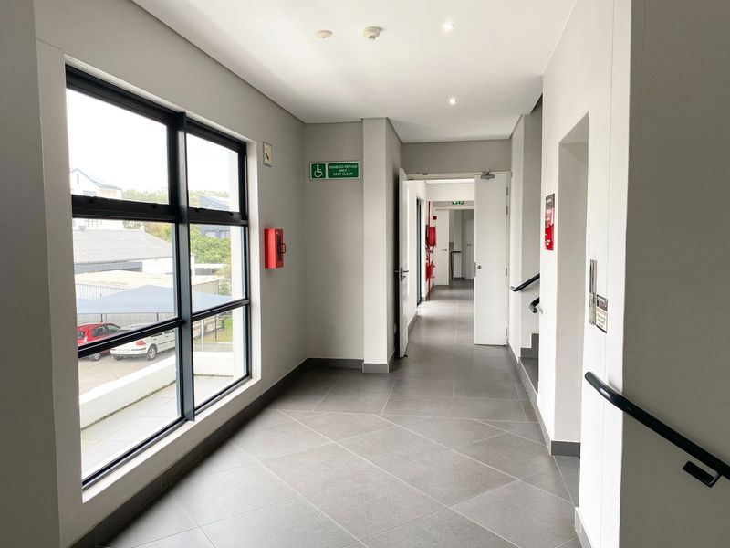 A clean, modern office hallway featuring large windows, tiled flooring, recessed lighting, and essential fire safety infrastructure.