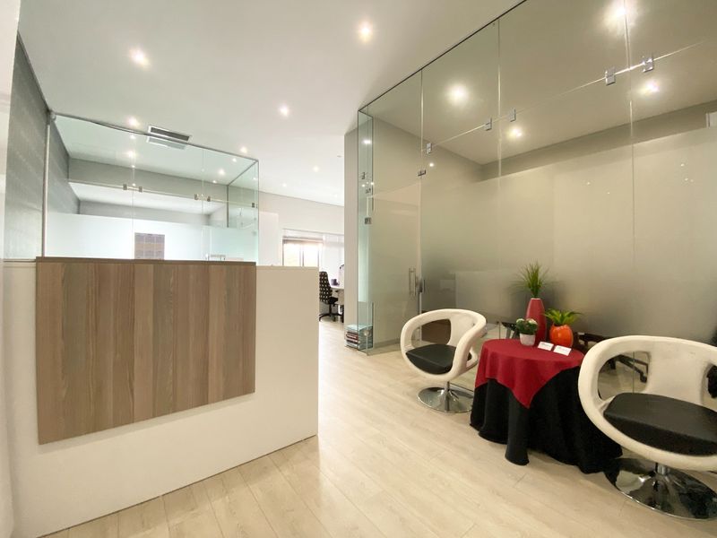 Modern office space featuring contemporary glass partitioning, recessed downlighting, and light-toned laminate flooring, creating a professional and bright work environment.