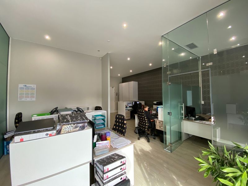 Modern office space featuring glass partition walls, recessed lighting, and light-toned laminate flooring, providing a professional and bright working environment.