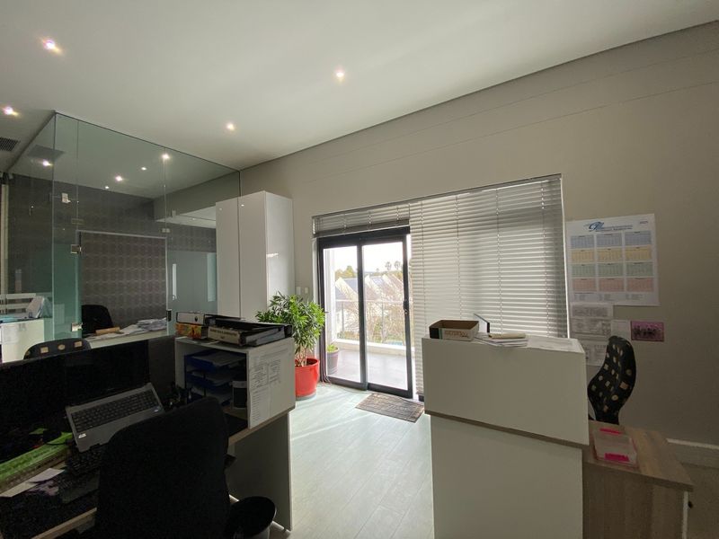 Modern office space featuring a glass partition, built-in cabinetry, and a sliding door leading to a balcony with natural light.