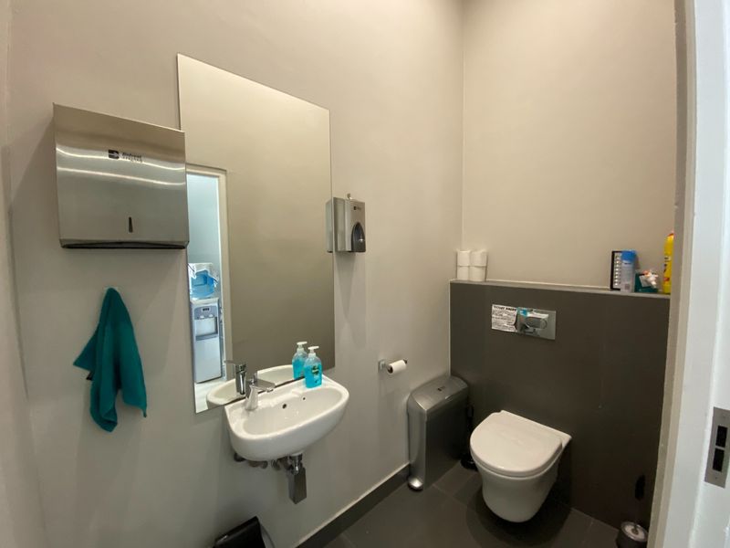 A clean, functional office restroom featuring a wall-mounted basin, modern wall-hung toilet, and neutral tiled finishes.