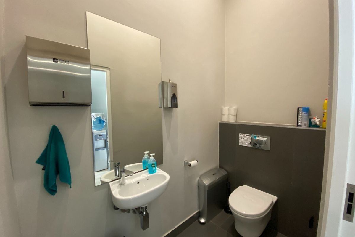 A clean, functional office restroom featuring a wall-mounted basin, modern wall-hung toilet, and neutral tiled finishes.