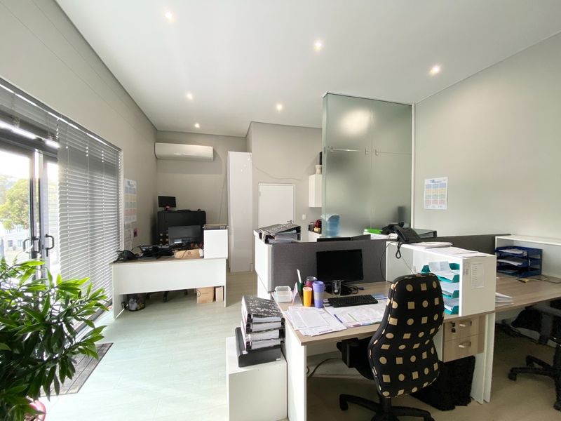 A well-lit office space featuring a glass partition, split-system air conditioning, and large sliding glass doors with venetian blinds.