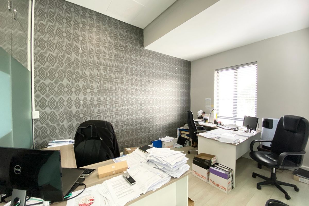 A functional office space featuring a decorative patterned accent wall, laminate flooring, and natural light provided by a window with venetian blinds.