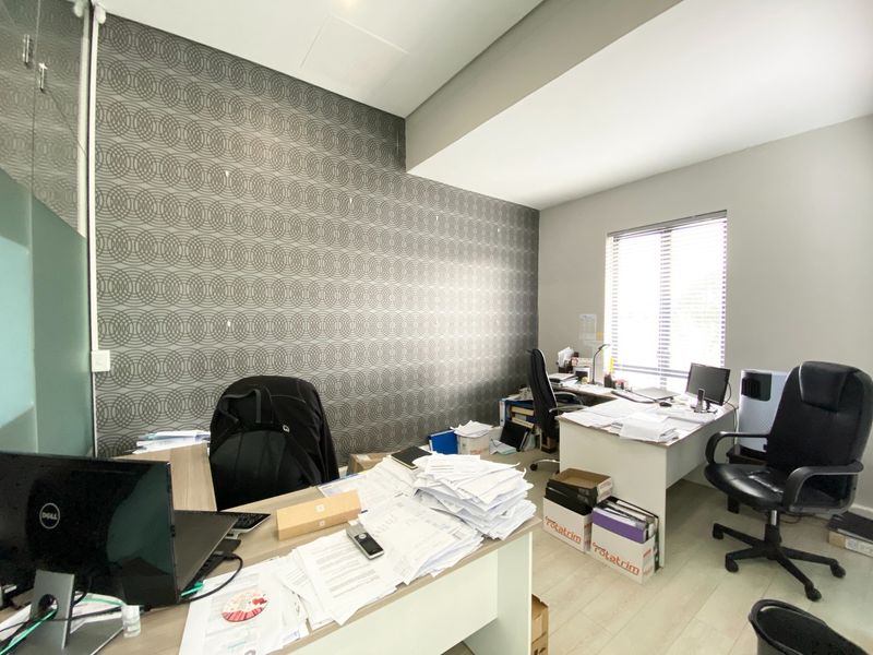A functional office space featuring a decorative patterned accent wall, laminate flooring, and natural light provided by a window with venetian blinds.