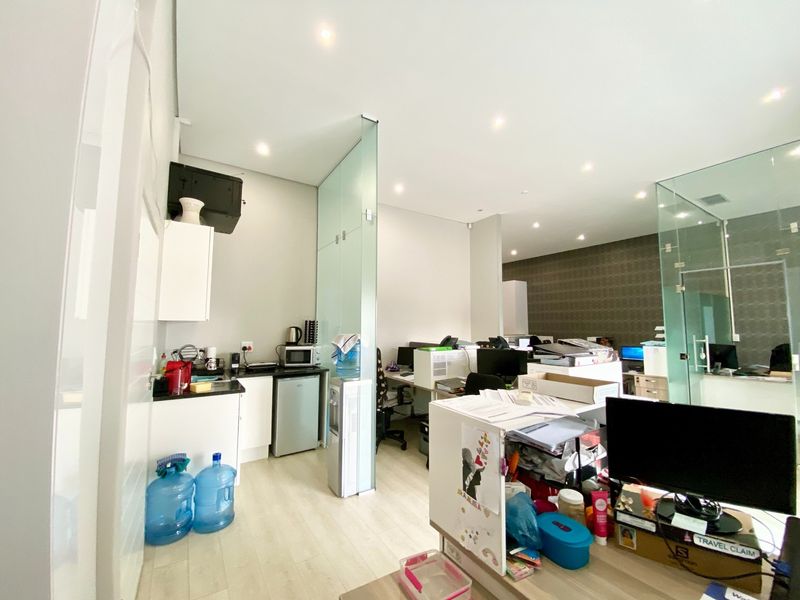 Modern office space featuring glass partitions, recessed lighting, laminate flooring, and a compact kitchenette area with built-in cabinetry.