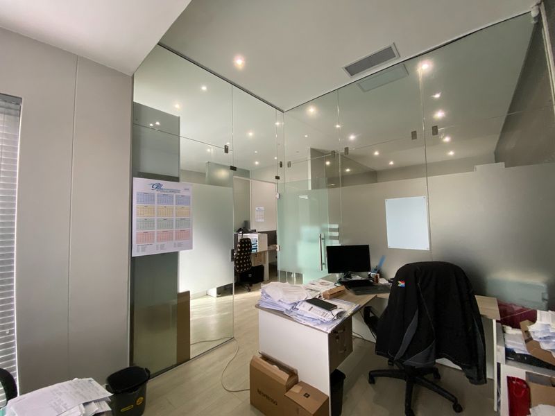 Modern office space featuring contemporary glass partition walls, recessed lighting, and integrated air conditioning, providing a professional and bright work environment.