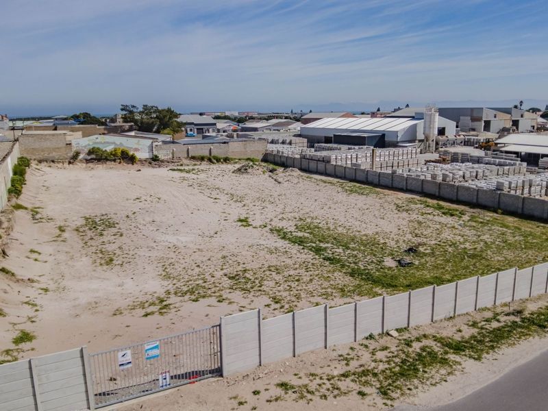 Aerial view of a vacant commercial plot featuring perimeter walling and gated access, situated in an established industrial area.