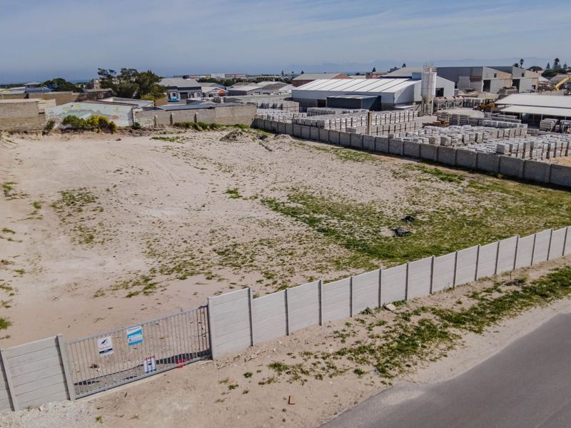 An aerial view of a vacant commercial plot enclosed by perimeter walls and a metal gate, situated in an industrial area.