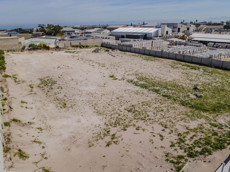 An aerial view of a vacant commercial land plot featuring perimeter boundary walls and a sandy, undeveloped surface in an industrial area.