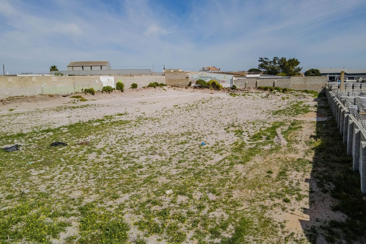 An expansive vacant commercial plot featuring perimeter masonry boundary walls and unimproved sandy ground surface.