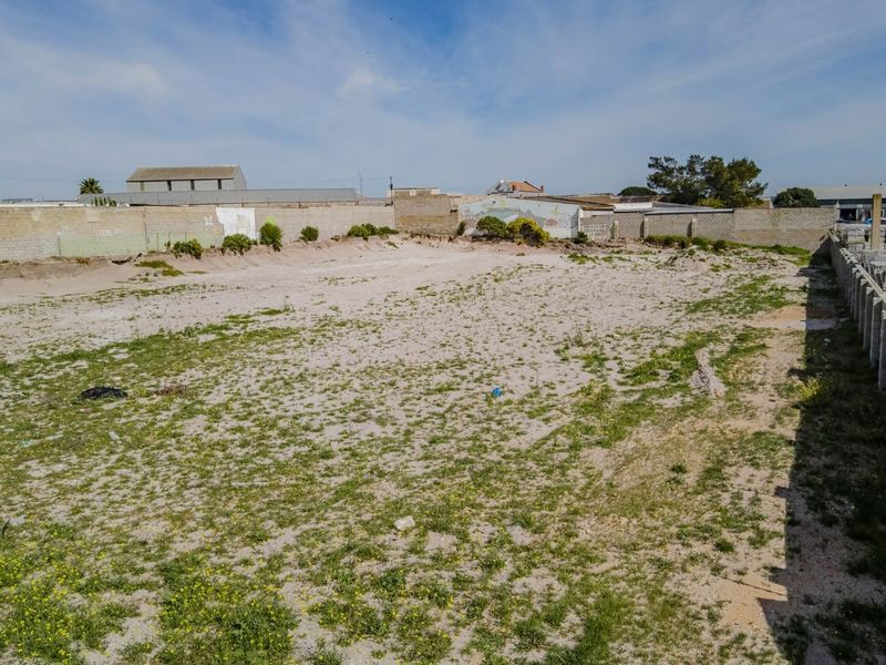 An expansive vacant commercial plot featuring perimeter masonry boundary walls and unimproved sandy ground surface.