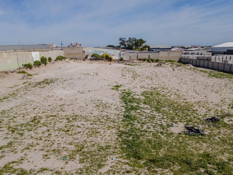 An elevated view of a vacant commercial plot featuring a sandy surface and enclosed by perimeter boundary walls.