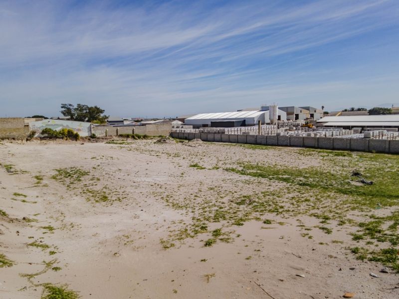 A vacant commercial land plot featuring a sandy surface and enclosed by a perimeter boundary wall in an industrial area.
