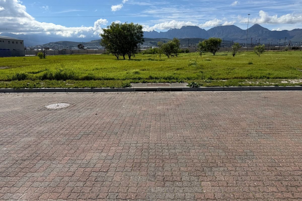 A view of a vacant commercial plot featuring paved street access, a stormwater drain, and mountain views in the background.
