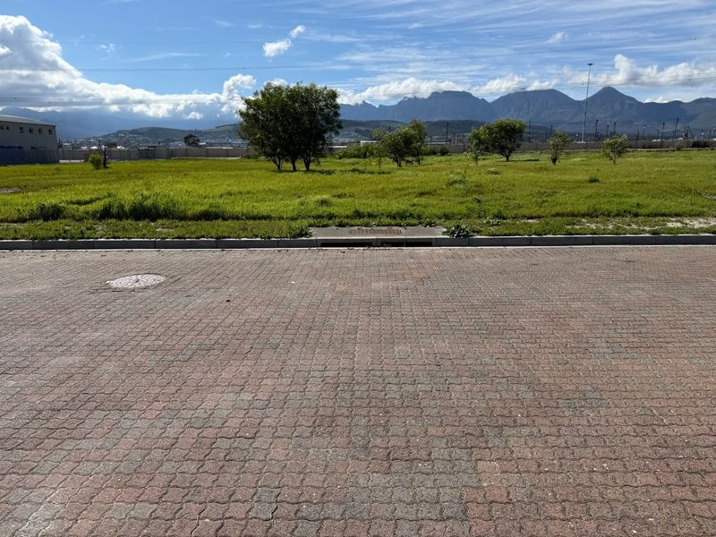 A view of a vacant commercial plot featuring paved street access, a stormwater drain, and mountain views in the background.