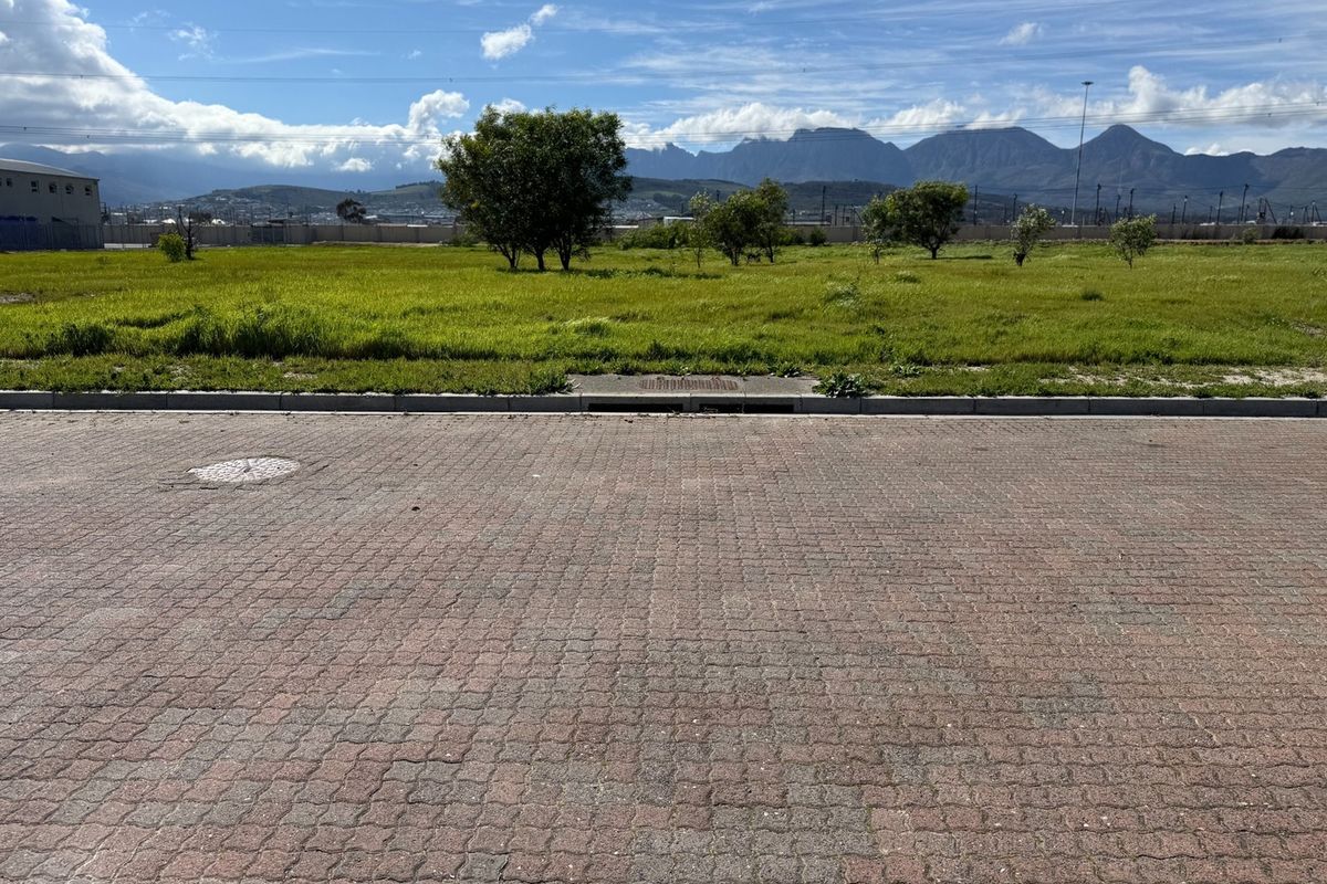 A view of a vacant commercial land plot featuring paved street access, established kerbing, and mountain views in the background.