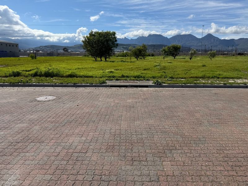 A view of a vacant commercial land plot featuring paved street access, established kerbing, and mountain views in the background.