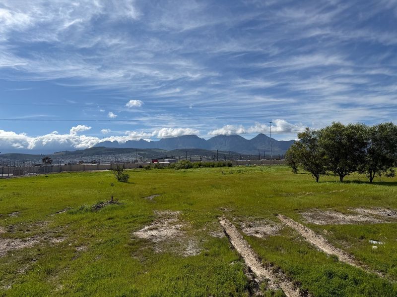 A wide-angle view of the vacant commercial land featuring open grassland, perimeter fencing, and scenic mountain views in the background.