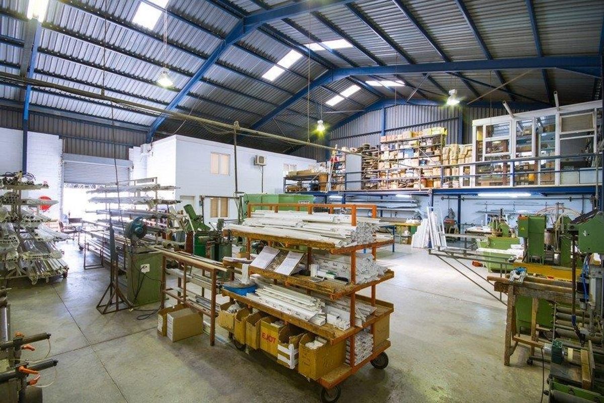 Spacious industrial workshop featuring a high-clearance steel portal frame, concrete flooring, integrated mezzanine level, and natural light provided by roof skylights.