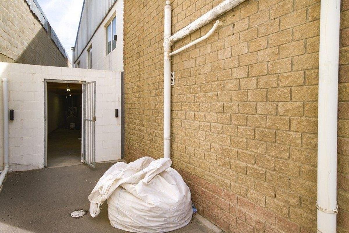 Rear exterior view of the industrial property featuring exposed brick walls, external drainage infrastructure, and a secure access gate.