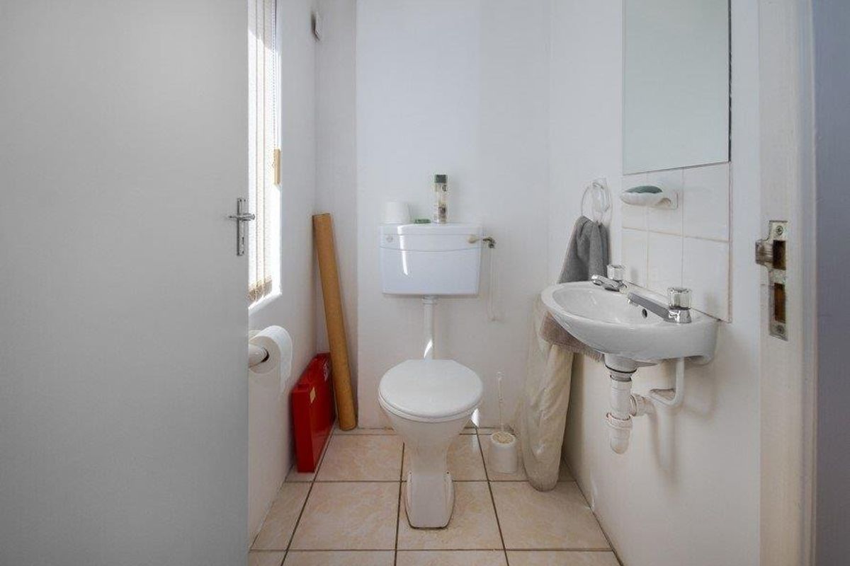 A compact bathroom featuring a standard toilet, wall-mounted basin, and tiled flooring, requiring some cosmetic updates to improve its overall condition.