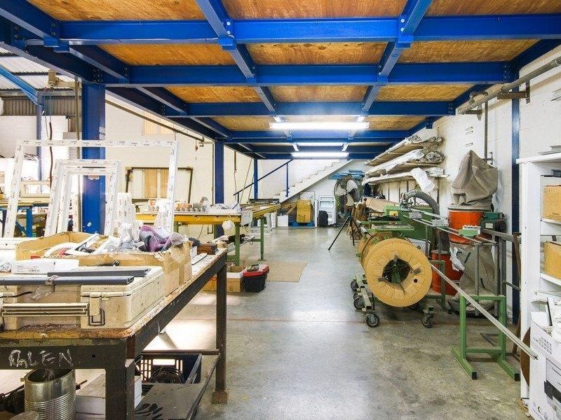 Spacious industrial workshop area featuring a mezzanine level, concrete flooring, and functional overhead lighting, suitable for manufacturing or storage operations.