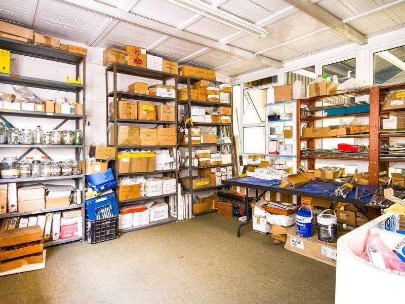 A functional industrial utility or storage space featuring extensive metal shelving, exposed ceiling structure, and ample natural light through large windows.