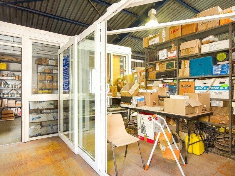 Industrial utility or storage space featuring metal shelving units, sliding glass partitions, and exposed roof structure, suitable for organized inventory management.