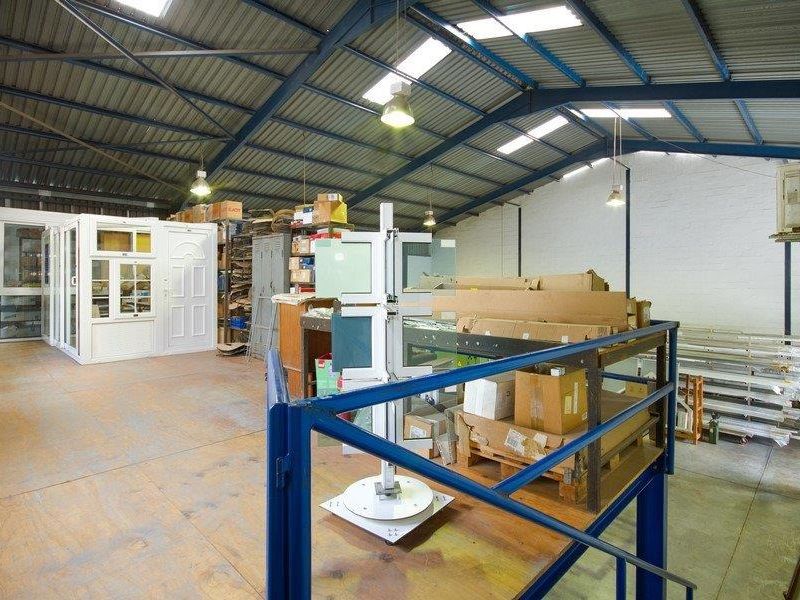 Spacious industrial utility area featuring exposed steel roof trusses, skylights, concrete flooring, and a mezzanine level with steel balustrading.