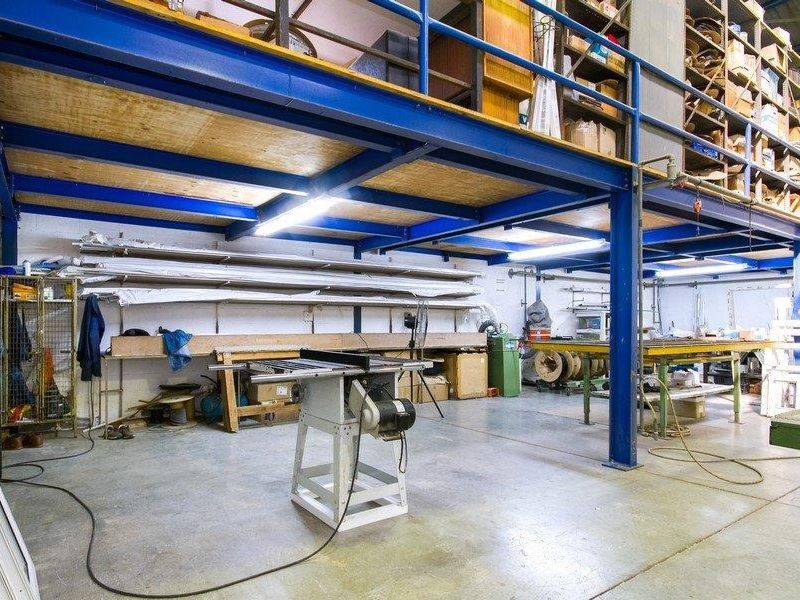 Industrial utility space featuring a mezzanine level with steel support structure, concrete flooring, and integrated shelving suitable for workshop or storage operations.