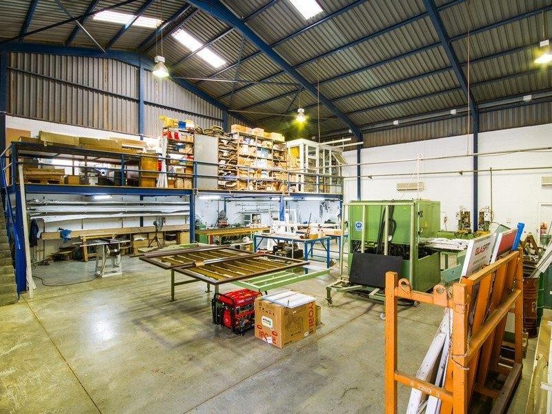Spacious industrial workshop featuring a mezzanine level, high ceilings with exposed steel trusses, skylights, and durable concrete flooring suitable for manufacturing or storage.