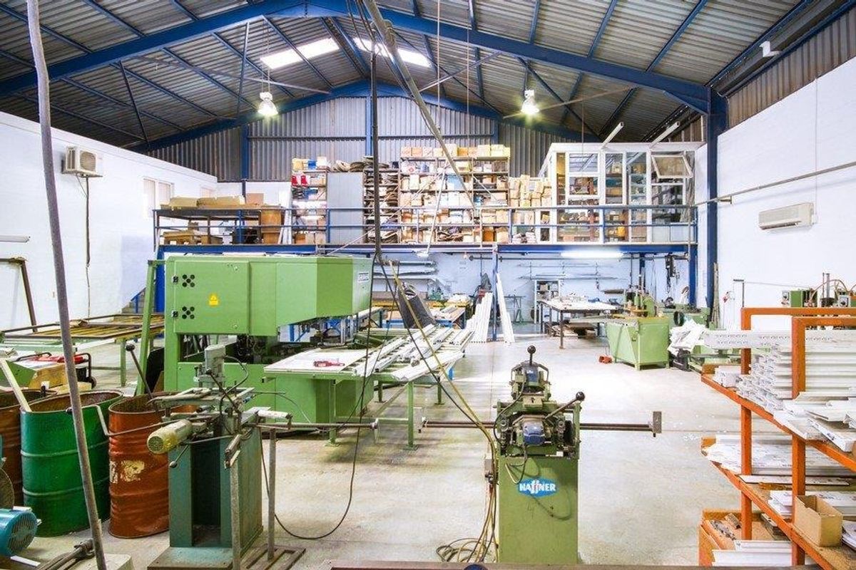 Spacious industrial workshop featuring high ceilings with exposed steel trusses, a mezzanine storage level, and integrated air conditioning units.
