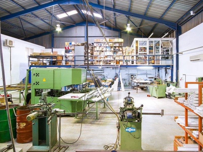 Spacious industrial workshop featuring high ceilings with exposed steel trusses, a mezzanine storage level, and integrated air conditioning units.