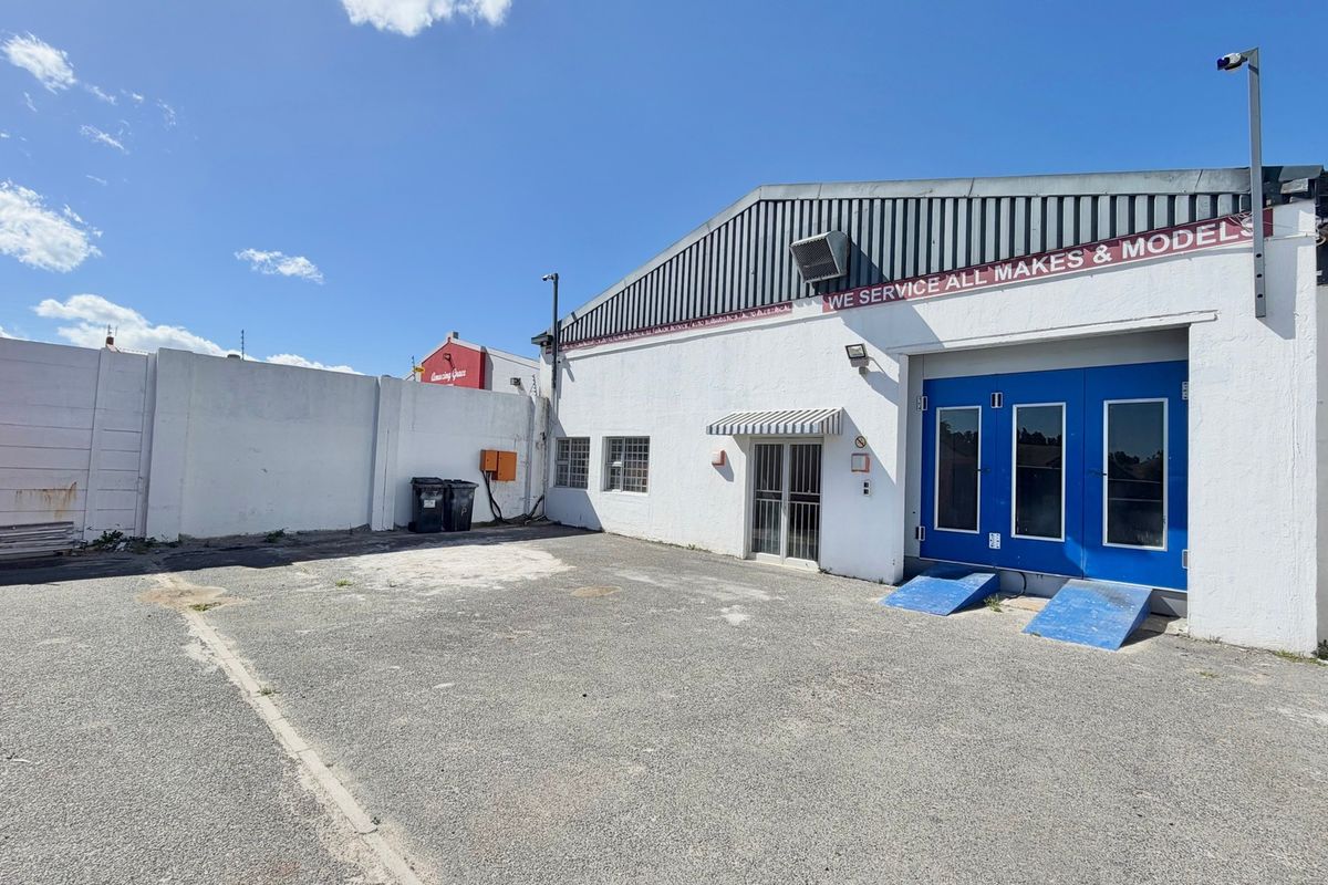 Industrial rear yard area featuring asphalt surfacing, perimeter walling, and access to the main workshop facility with blue security doors.