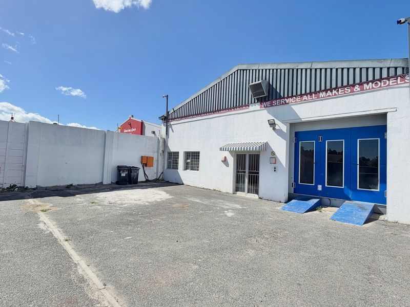 Industrial rear yard area featuring asphalt surfacing, perimeter walling, and access to the main workshop facility with blue security doors.