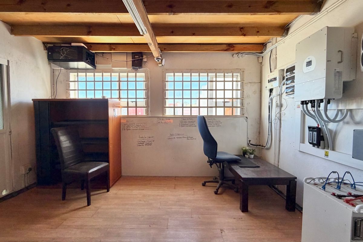 Functional office space featuring exposed timber ceiling beams, security-barred windows, and integrated solar power infrastructure with visible electrical distribution components.