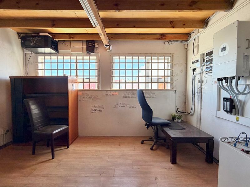 Functional office space featuring exposed timber ceiling beams, security-barred windows, and integrated solar power infrastructure with visible electrical distribution components.