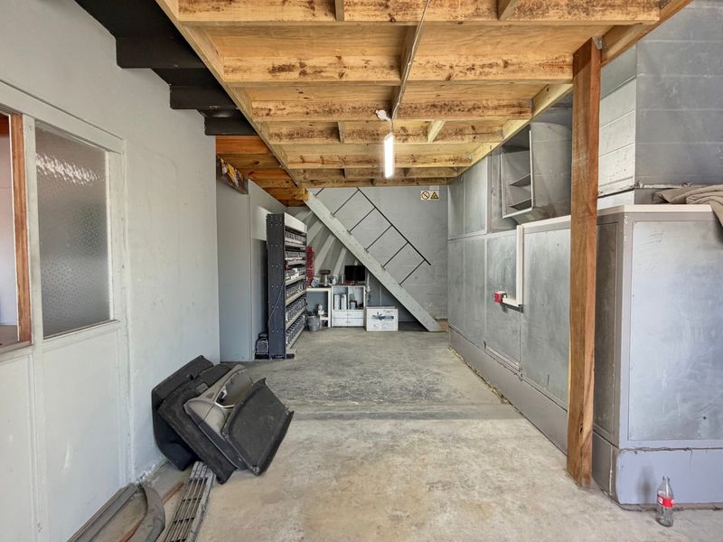 Industrial utility space featuring exposed timber ceiling joists, concrete flooring, and a metal staircase, suitable for workshop or storage use.